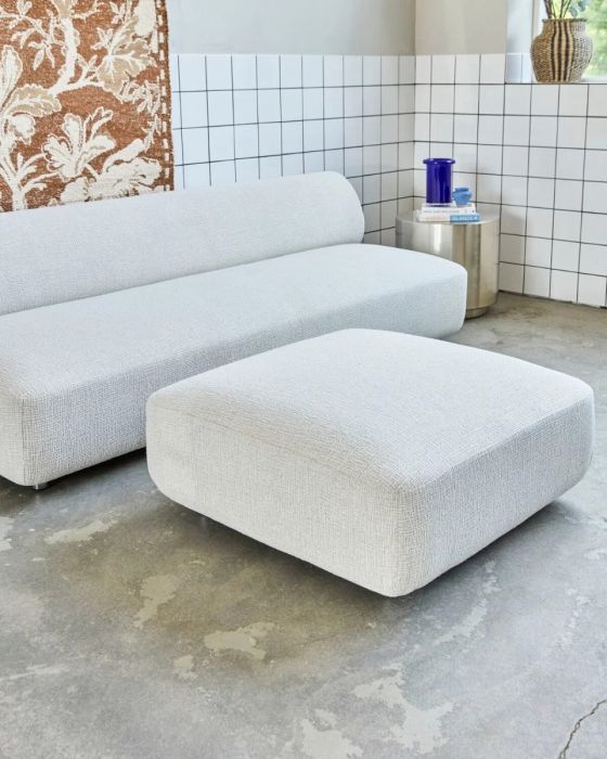 Puf en madera contrachapada tapizada en tejido blanco roto con patas de aluminio plateado.