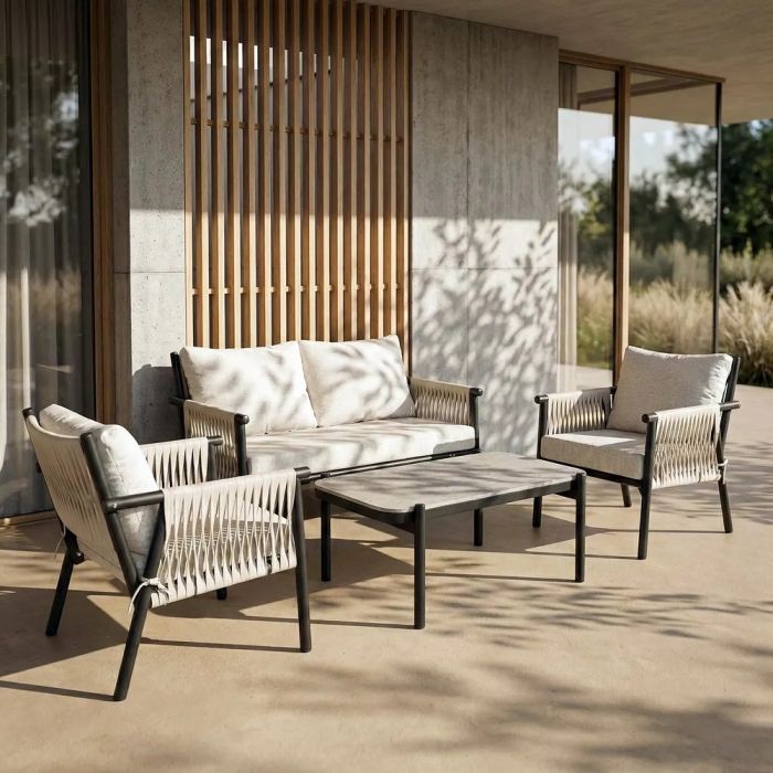 Conjunto de sofá jardín en ratán, acero color negro, cojines crema y piedra gris.