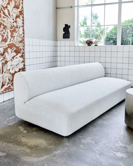Sofá en madera contrachapada tapizada en tejido blanco roto y patas de acero plateado.